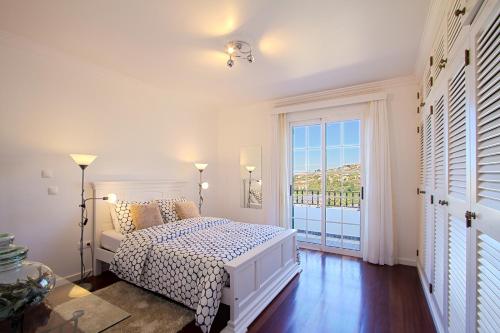 a white bedroom with a bed and a large window at Casa Conduto in Ponta do Sol