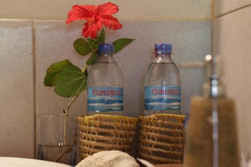 The Beach Crab Resort في Pangani: زجاجتان من الماء و وردة حمراء في مزهرية