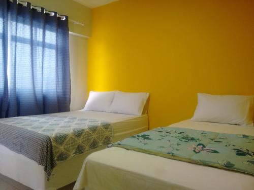 two beds in a room with yellow walls and a window at Pousada Itararé in Campina Grande