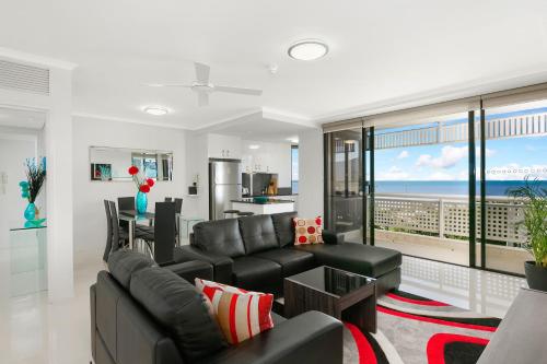 a living room with a black leather couch and a kitchen at Cairns Luxury Seafront Apartment in Cairns