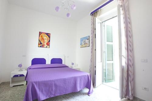 een witte slaapkamer met een paars bed en een raam bij Casa Baia Luna in Ponza