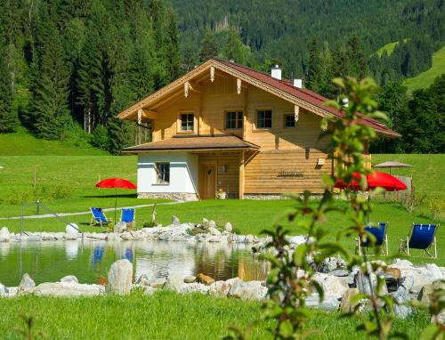 a log cabin with chairs and a pond in front of it at Lehenriedl Chalet in Wagrain