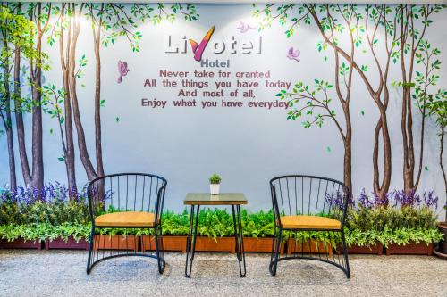 a table and two chairs in front of a wall with trees at Livotel Hotel Hua Mak Bangkok in Bangkok
