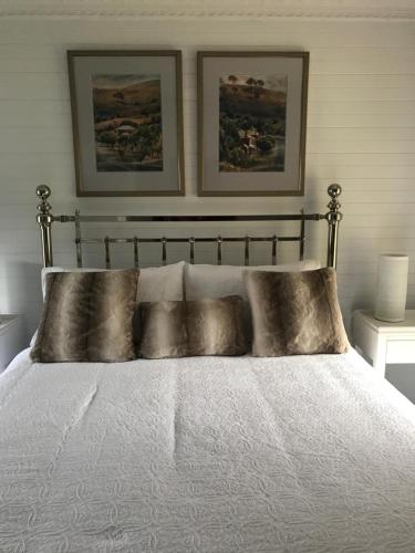 a bedroom with a white bed with two pictures on the wall at Drayshed cottage in Blayney