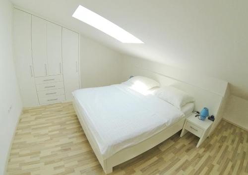 a white bedroom with a bed and a night stand at Apartments Barbati in Novalja