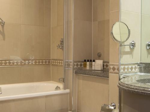 bagno con doccia, vasca e specchio di Nutfield Priory Hotel & Spa a Redhill