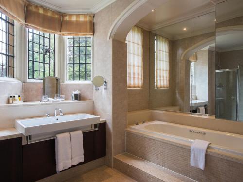 bagno con vasca, lavandino e specchio di Rhinefield House Hotel a Brockenhurst