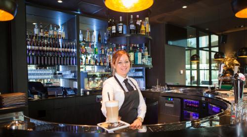 a woman standing behind a bar with a drink at Van der Valk Hotel Utrecht in Utrecht