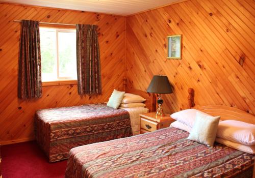 two beds in a room with wooden walls and a window at Hidden Acres Cottages in Cavendish