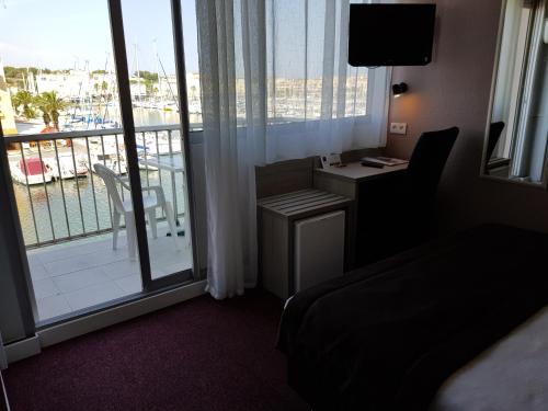 a hotel room with a bed and a desk and a balcony at Hôtel Port Beach in Gruissan
