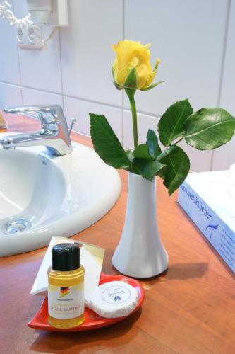 a yellow rose in a white vase on a bathroom counter at Bertricher Hof Hotel Garni in Bad Bertrich