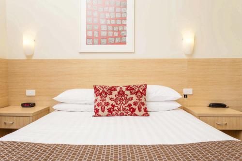 a bedroom with a bed with a red pillow on it at The Club Motel and Apartments in Wagga Wagga