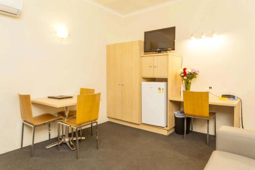 a room with a desk and a table and a refrigerator at The Club Motel and Apartments in Wagga Wagga