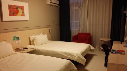 a hotel room with two beds and a red chair at Jinjiang Inn Xiamen Xiang'an Maxiang in Xiamen