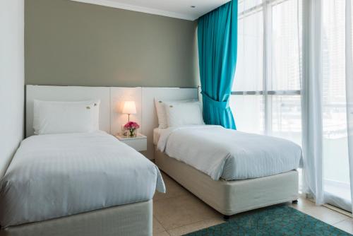 two beds in a bedroom with blue curtains and a window at Jannah Place Dubai Marina in Dubai