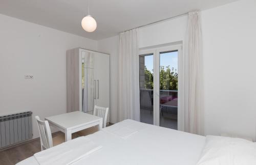 a white bedroom with a bed and a table and a window at Rooms Villa Bašica in Saplunara
