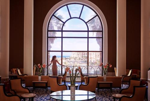 une femme debout devant une grande fenêtre dans l'établissement Corinthia Hotel St. George’s Bay, à San Ġiljan