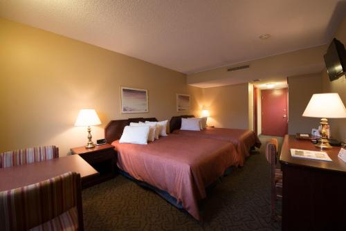 une chambre d'hôtel avec un lit, deux tables et des lampes dans l'établissement Assiniboine Gordon Inn on the Park, à Winnipeg