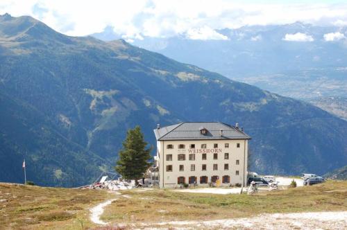 a building on a hill with mountains in the background at Hôtel Weisshorn sur St-Luc 2337m in Saint-Luc