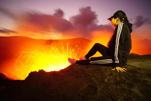 a woman sitting on a rock in front of a fire at Tanna Evergreen Resort & Tours in Tanna Island