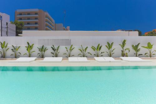 a row of white benches next to a swimming pool at White Apartments - Adults Only in Ibiza Town
