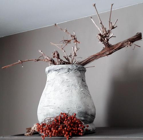 a white vase with branches and berries on a table at Hoeve Schevey in Mechelen
