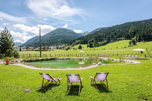 two chairs sitting in the grass in front of a pond at Almdorf Almlust in Flachau
