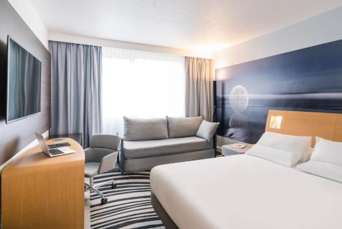 a hotel room with a bed and a chair at Novotel Saclay in Saclay