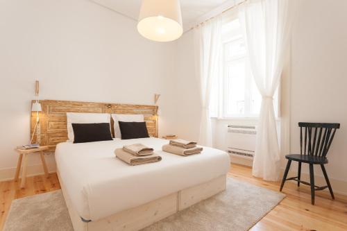 um quarto branco com uma grande cama branca e uma cadeira em FLH Bica Modern Flat with View em Lisboa