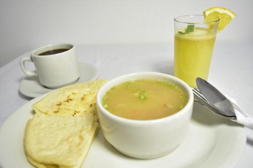 a bowl of soup on a plate with a tortilla and a drink at Hotel El Principe in Ocaña