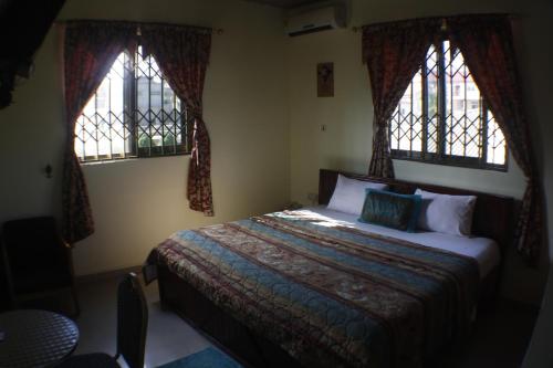 a bedroom with a bed and two windows at Dokua Royal Hotel in Accra