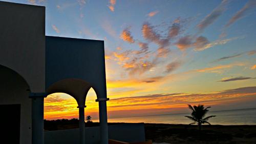 a sunset over the ocean with a building and a palm tree at Villa Star of the Sea in Barra de Navidad