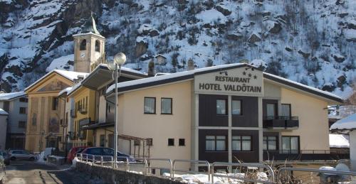 a hotel building with a clock tower in front of a mountain at Hotel Valdotain in Villeneuve