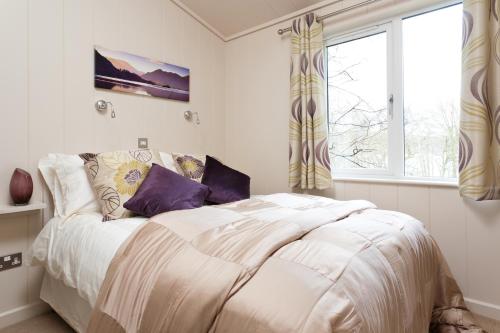 a bedroom with a bed with white sheets and purple pillows at Hill Of Oaks in Windermere