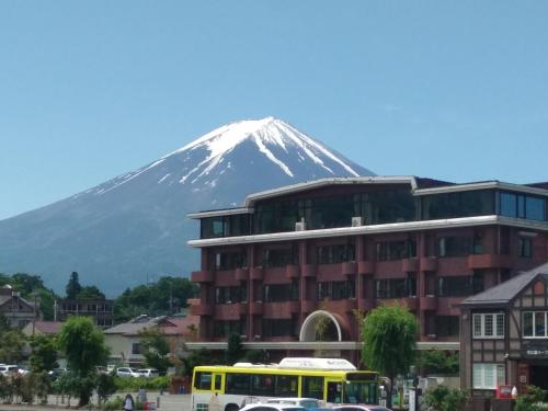 a snow covered mountain behind a building and a yellow bus at Shiki-no-Yado Fujisan in Fujikawaguchiko