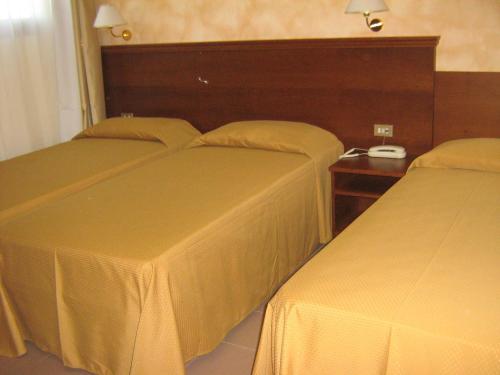 two beds in a hotel room with a table at Hostiliae Ciminiera Hotel in Ostiglia