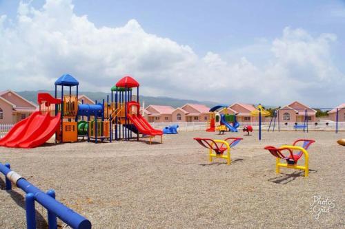 un parque infantil con toboganes coloridos y sillas en la arena en Caymanas Estate beautiful three bedroom house, en Spanish Town