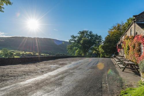 a dirt road with a building and the sun in the sky at Craven Shepherd Huts in Appletreewick