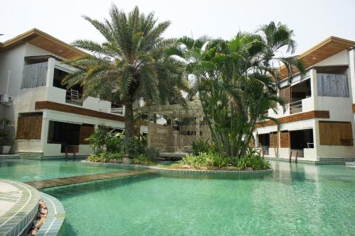 a swimming pool in front of a building with palm trees at The Hideaway Resort in Hua Hin