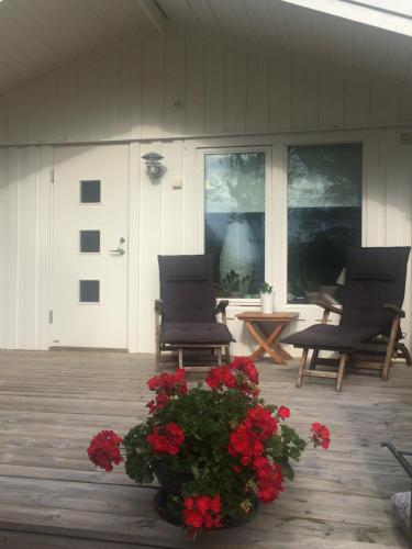 un porche con 2 sillas y una maceta de flores rojas en Lyckhus en Ljungskile