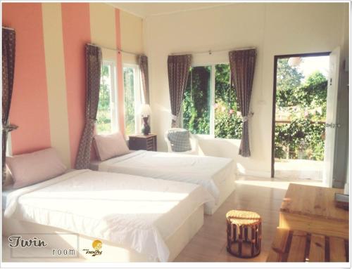 a bedroom with two beds and a table and windows at Thorfun Guesthouse in the Garden in Nakhon Ratchasima