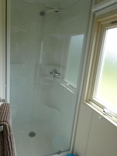 une douche avec une porte en verre à côté d'une fenêtre dans l'établissement Roulotte Bigoudenne, à Tréméoc