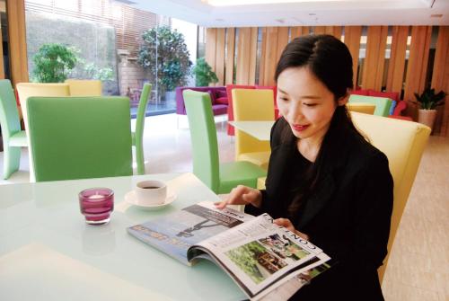 a woman sitting at a table reading a magazine at Century Hotel Taoyuan in Taoyuan