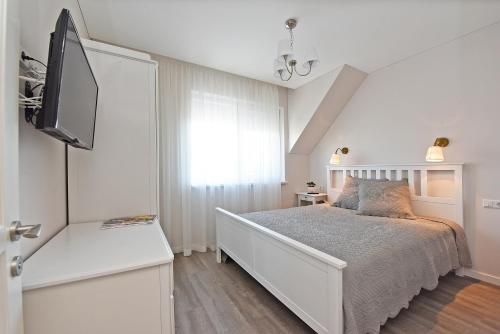 a white bedroom with a bed and a tv at Karklės namelis in Karklė