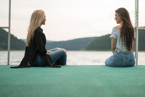 two women sitting on a dock next to the water at Pensiunea Vis Alpin Belis in Beliş