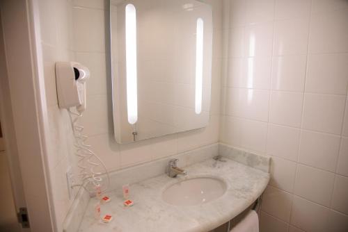 a bathroom with a sink with a mirror and a phone at ibis Joinville in Joinville