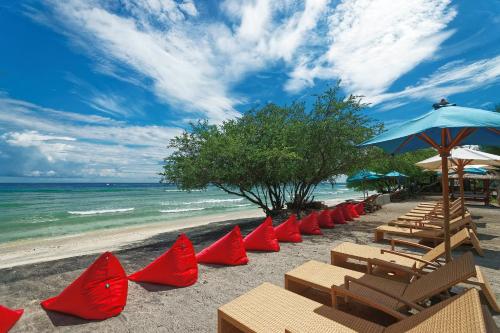 a row of red chairs and umbrellas on a beach at Jambuluwuk Oceano Gili Trawangan in Gili Trawangan