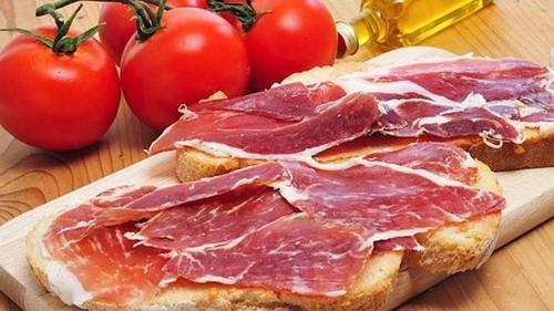 a piece of bread with bacon on it next to tomatoes at Bayo Lirola Hotel Balisa in Níjar