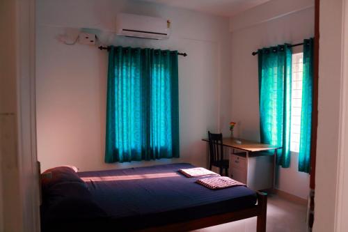 Cette chambre comprend un lit avec des rideaux bleus et un bureau. dans l'établissement EN Jays Residency (Service Apartments), à Kottayam