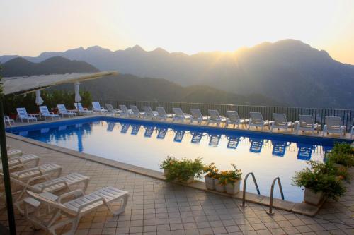 a hotel swimming pool with chairs and mountains in the background at Hotel Graal in Ravello